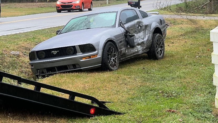 A gray Mustang on a roadside lawn with the flatbed ramp lowered beside it